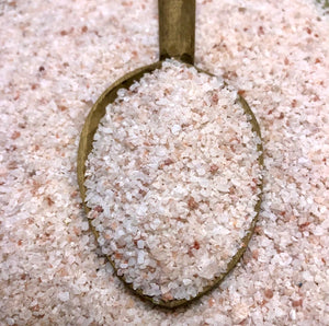This product image consists of a rustic dark wooden spoon, sitting on top of natural langbeinite. The langbeinite has soft pink tones with a crystal like in texture, similar to Himalayan sea salt.